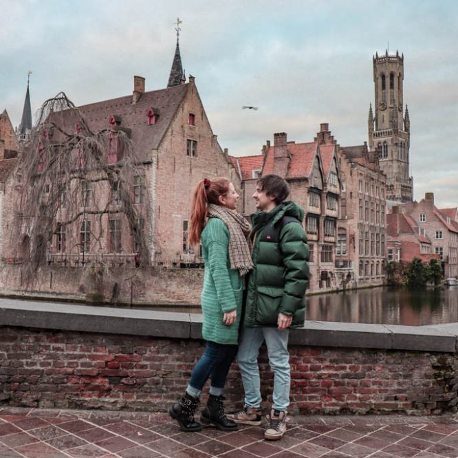 A couple posing in the medieval city of Bruges with view on one of the canals and the belfry tower