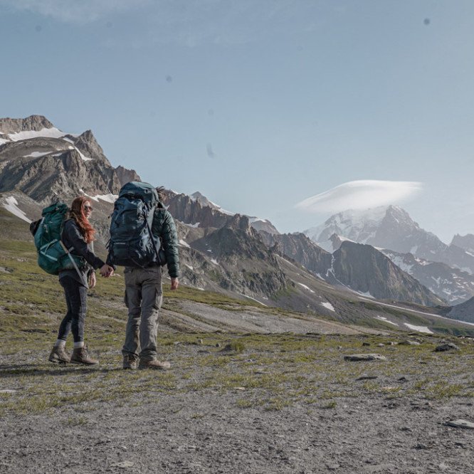 A couple holding hands wearing a big backpack while hiking the Tour du Mont-Blanc